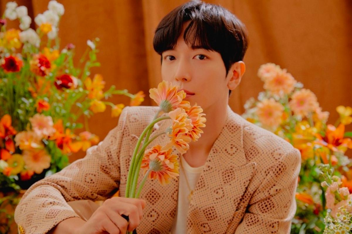 人物手持花束置身於色彩繽紛的花卉背景前，身穿花紋精美的西裝，洋溢著清新浪漫的氛圍。