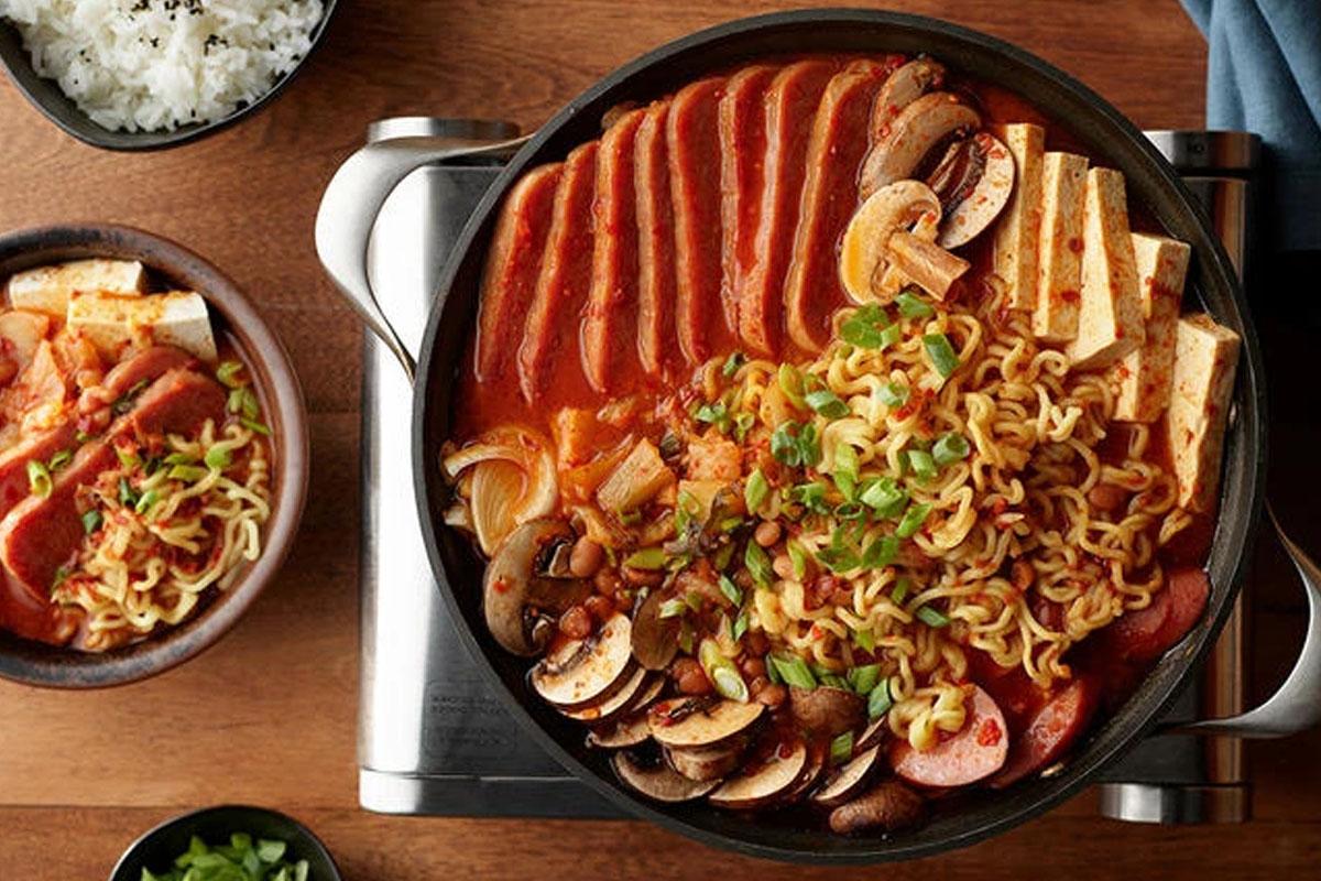 บูแดชิแกเกาหลีในหม้อเหล็ก มีสแปม เนื้อวัว และส่วนผสมอื่น ๆ วางอยู่ในชาม