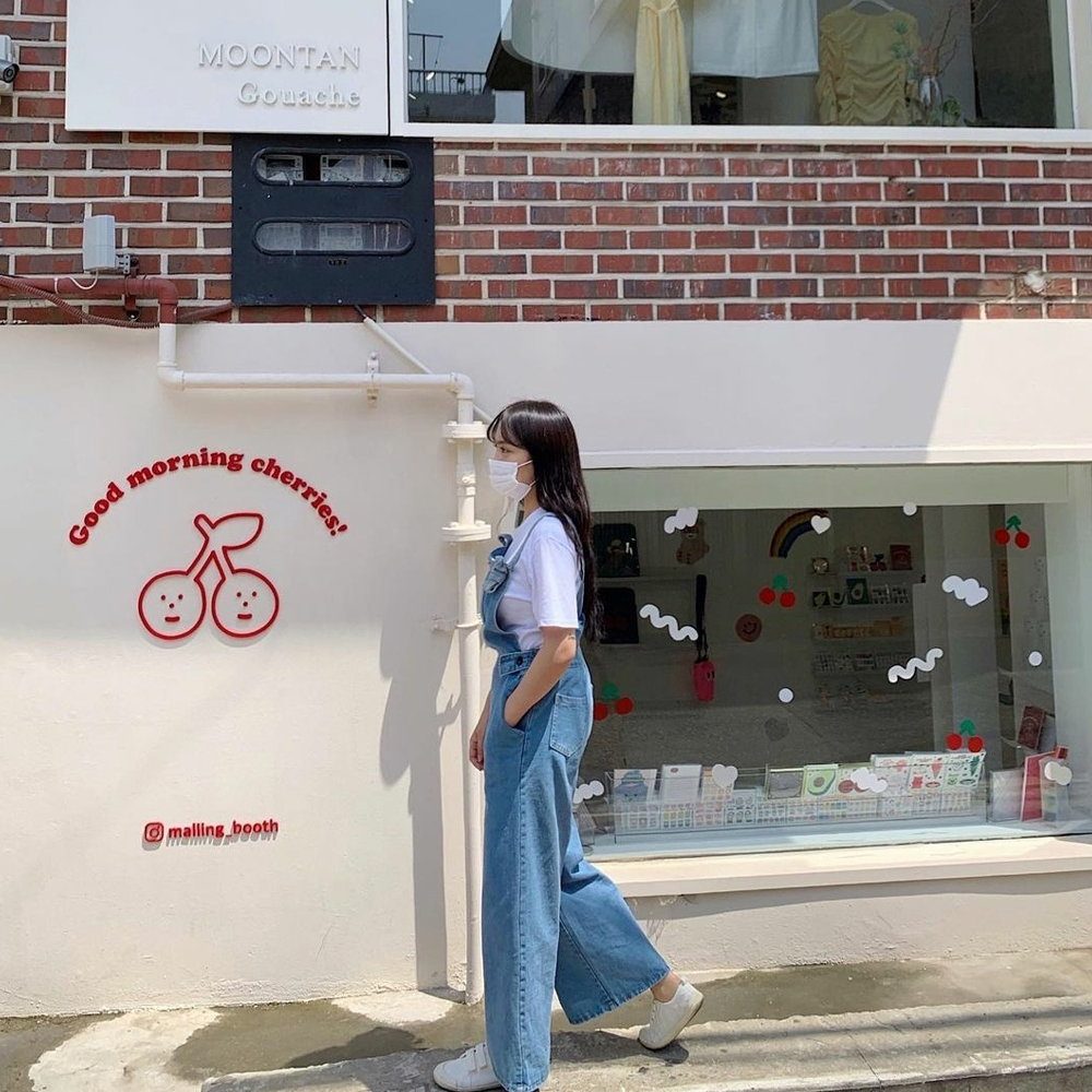 Fille marchant devant le mur blanc de Malling Booth avec une façade de cerises