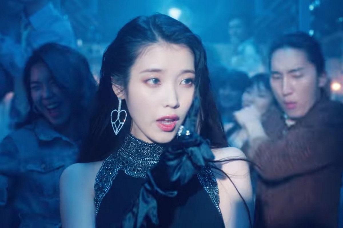 IU在《LILAC》MV中的舞台場景，一身華麗的晚裝，背景氛圍漸濃的藍光。