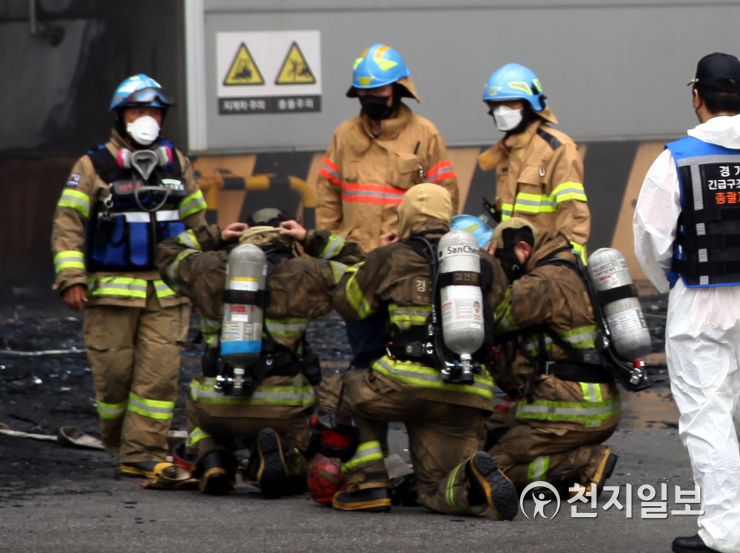 消防員在倉庫外部進行緊急協調。穿著防護服，裝備齊全。