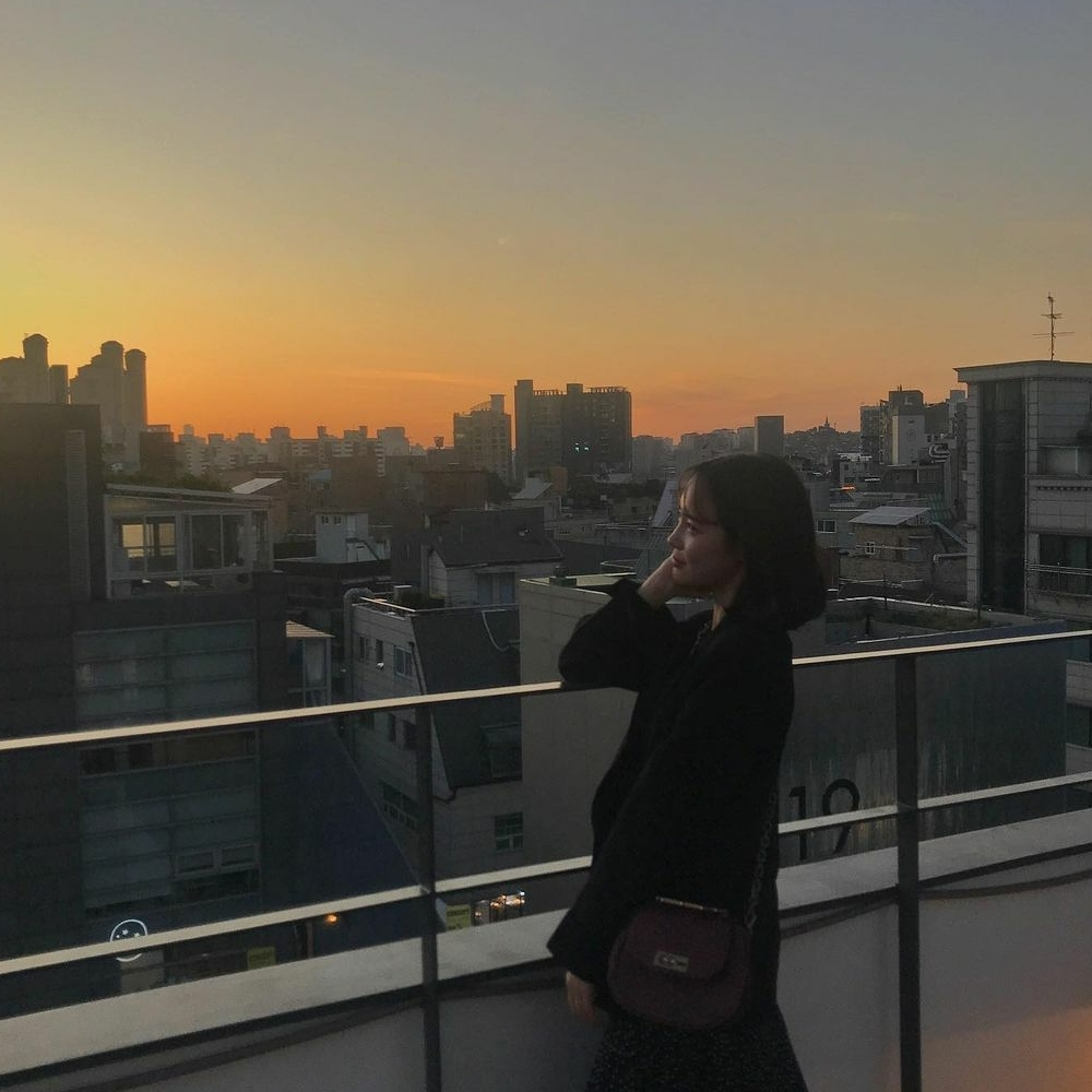 Wanita duduk menikmati pemandangan di teras atap Garogolmok Seoul di sore hari dengan langit cerah.