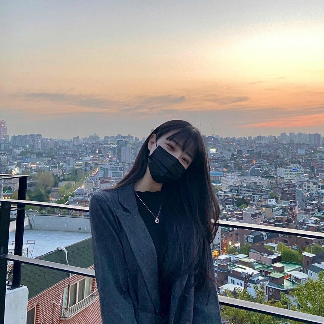 girl with long hair wearing black mask standing infront of a view of Seoul at Cafe Moonee rooftop