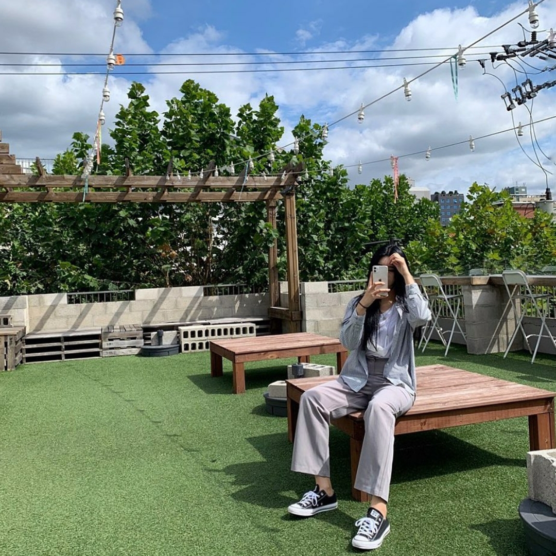 girl wearing converse sitting on a wooden desk at Cafe Skön rooftop with artificial grass