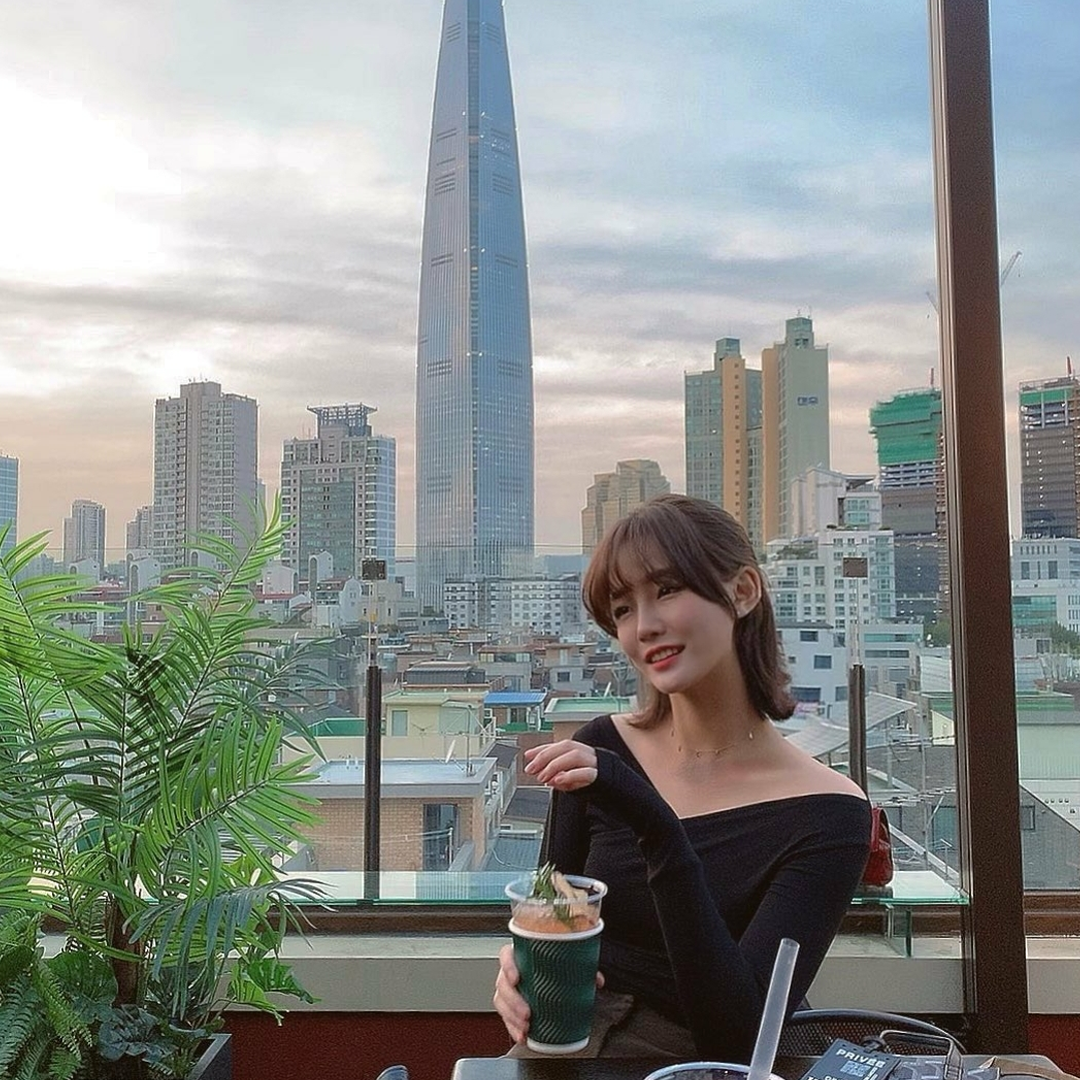 girl with short hair sitting on the rooftop of Seoulism with a view of the Lotte World Tower