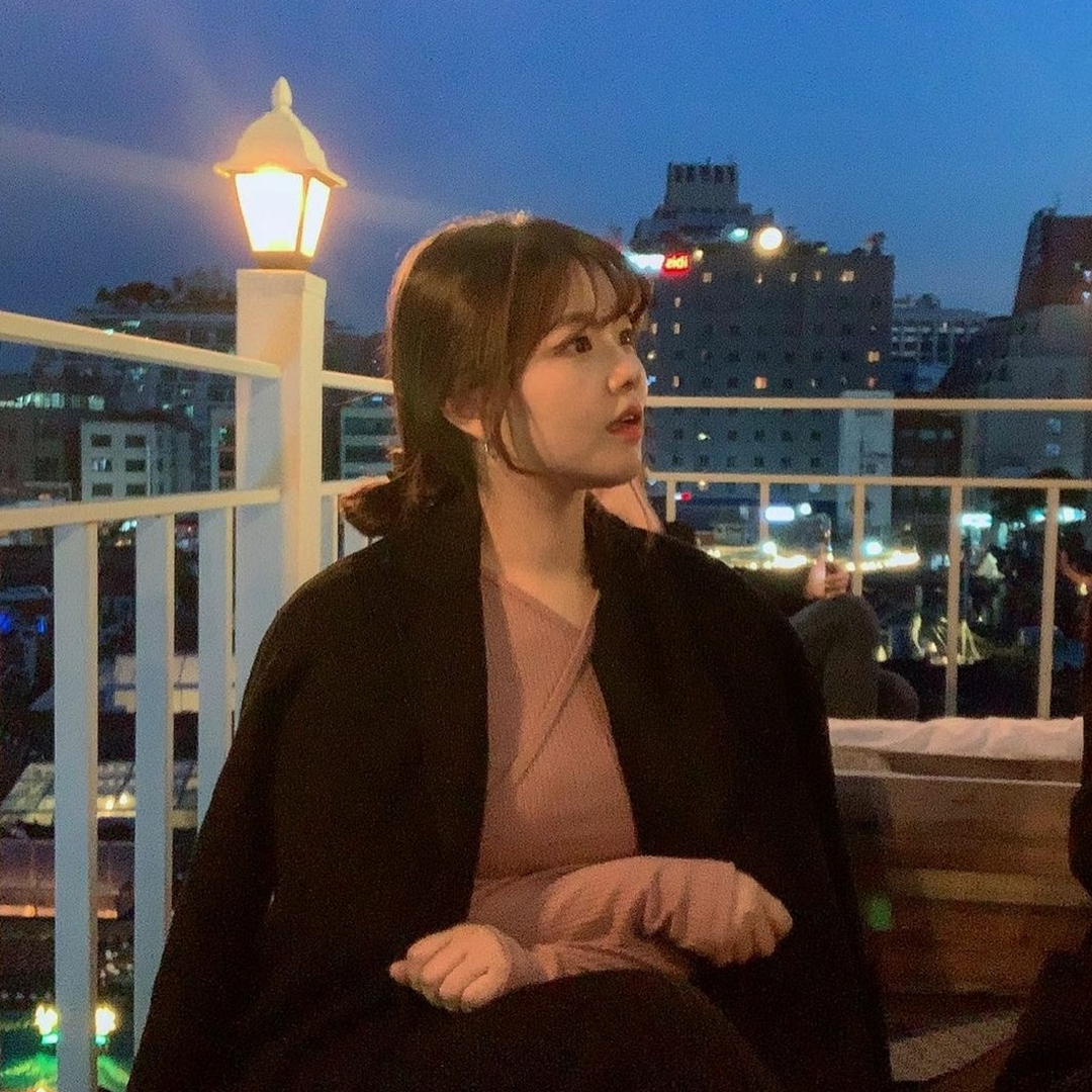 Korean girl with bangs and low bun sitting on the rooftop of Hotel Seine at night