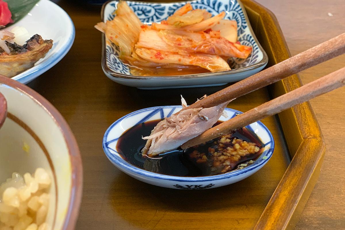 Customer dipping piece of grilled fish in soy sauce