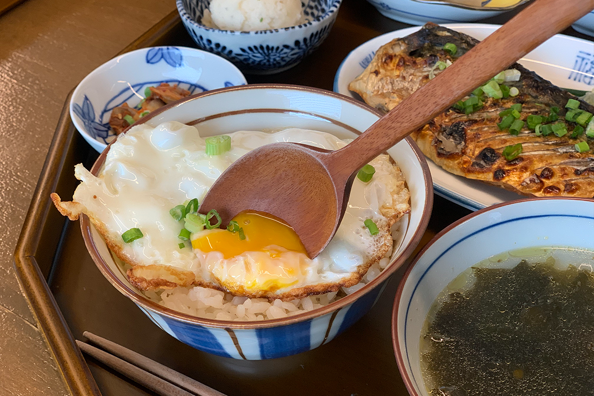 盛滿白飯和煎蛋的碗，擺放在木製託盤上，旁邊有青花魚和湯。