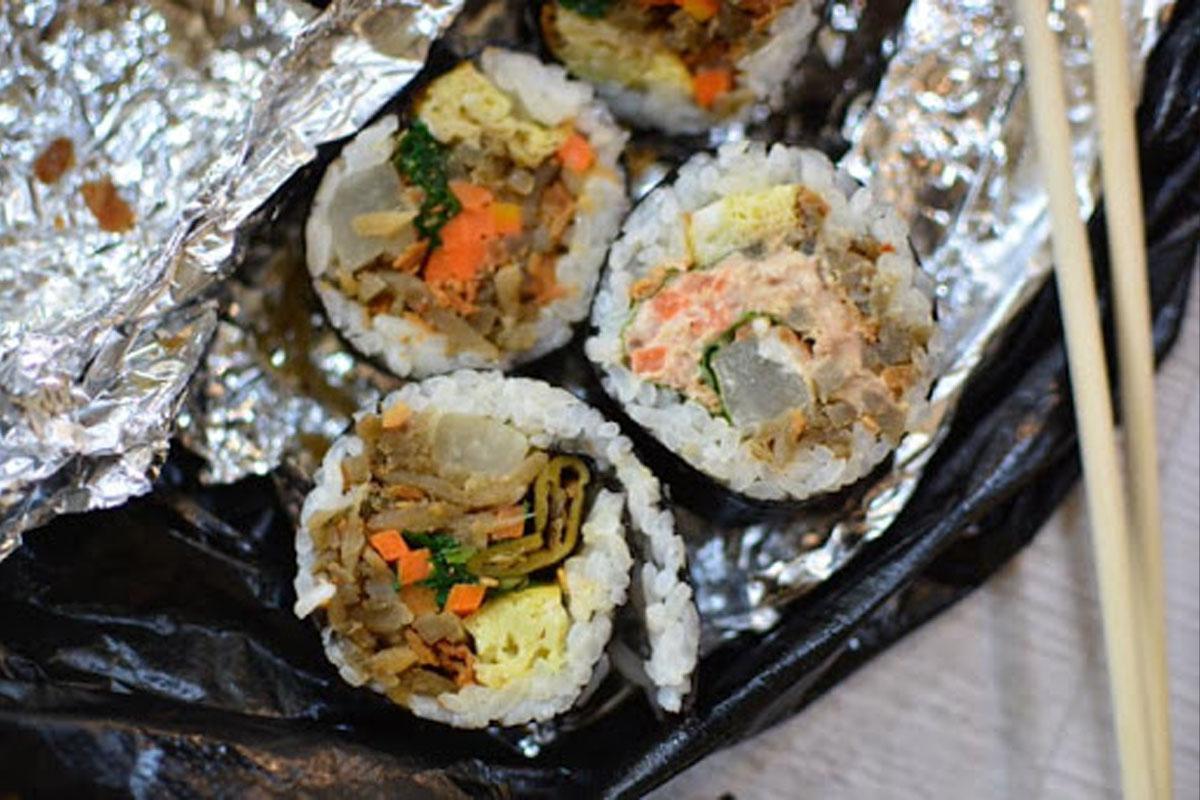 ซูชิกิมบับห่อในฟอยล์บนจานพร้อมตะเกียบทางด้านบน แสดงถึงเหตุการณ์เกี่ยวกับอาหารในเรื่องราวของ APRIL