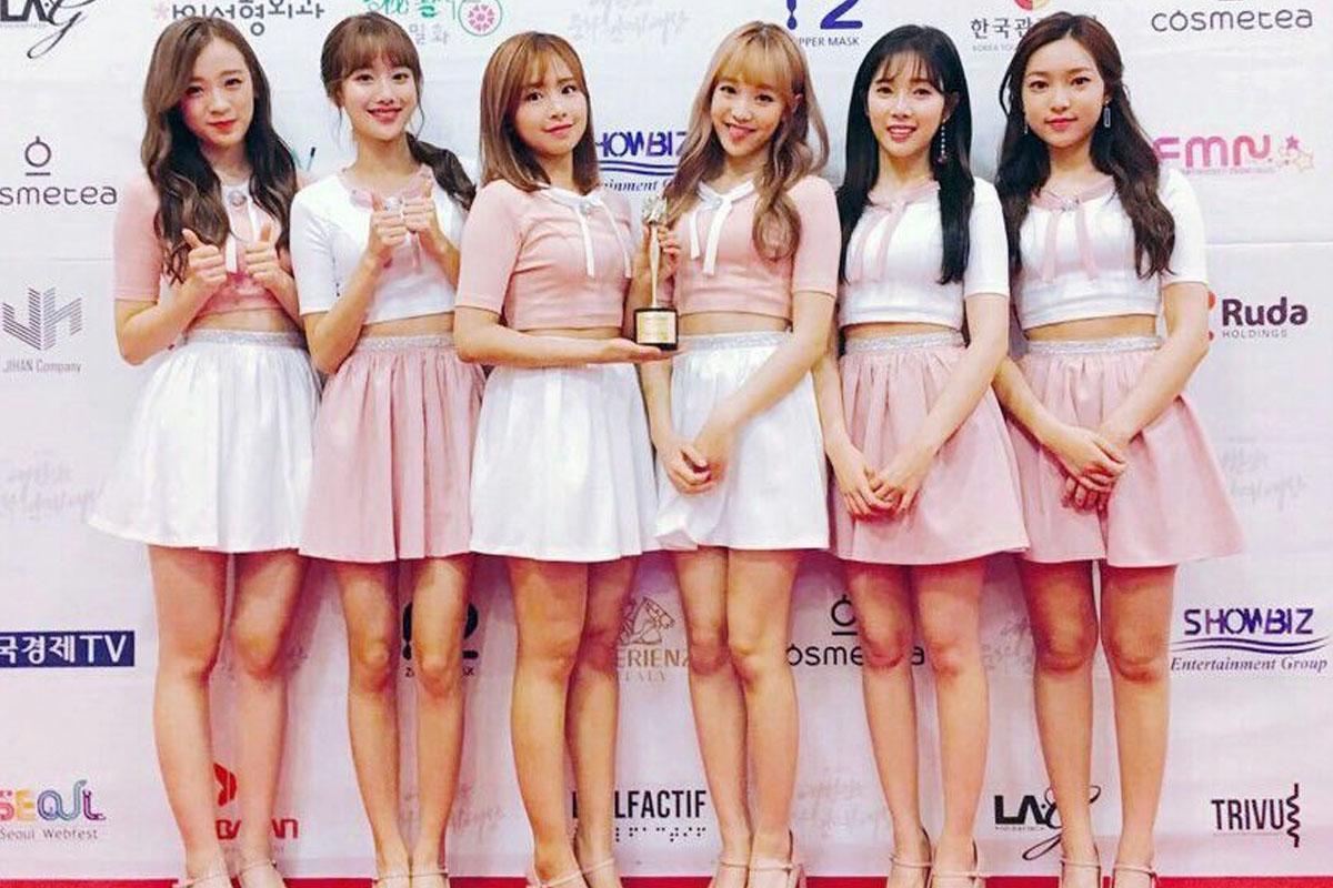 ภาพสมาชิกวง APRIL ในชุดสีชมพูและสีขาวขณะถือรางวัลบนเวทีเซรามิก