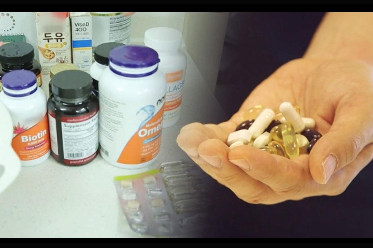 ขวดวิตามินเสริมสุขภาพหลายชนิดในเกาหลีที่วางอยู่บนโต๊ะข้างๆมือที่ถือวิตามินหลากสีสันในปริมาณมาก