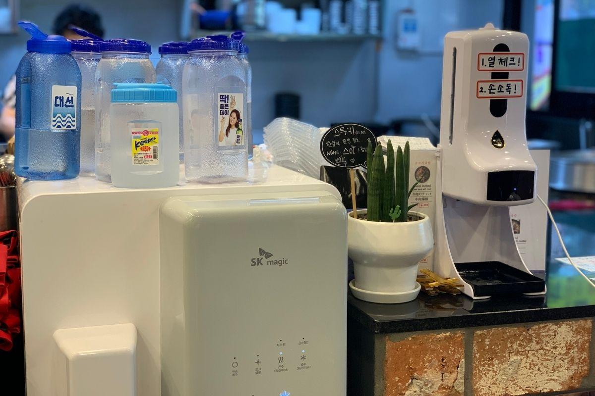 Kệ chứa nước rửa tay và máy đo nhiệt độ tại Haeundae Wonjo Halmae Gukbap, Busan, Hàn Quốc.