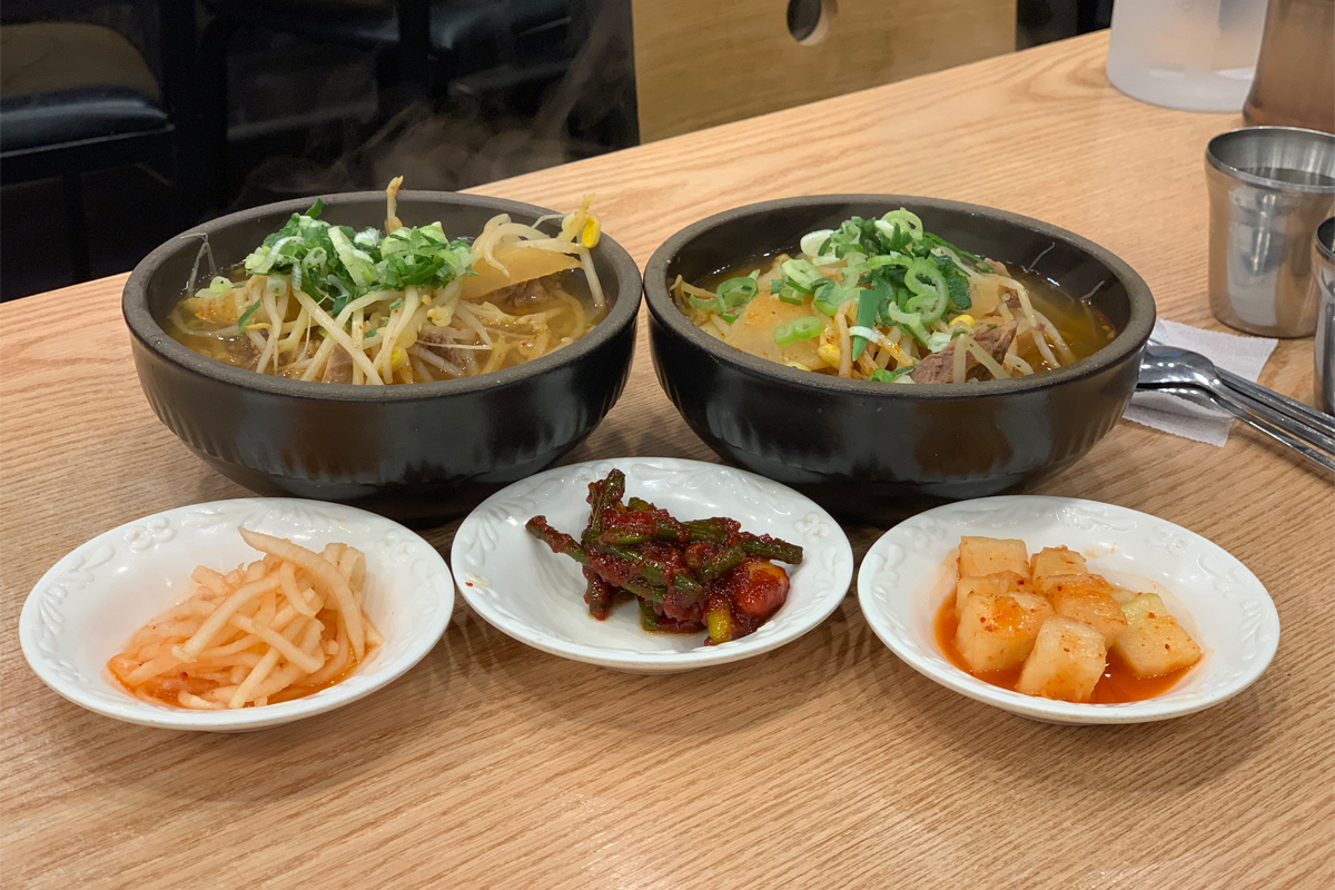 Two bowls of soup with rice and side dishes on table