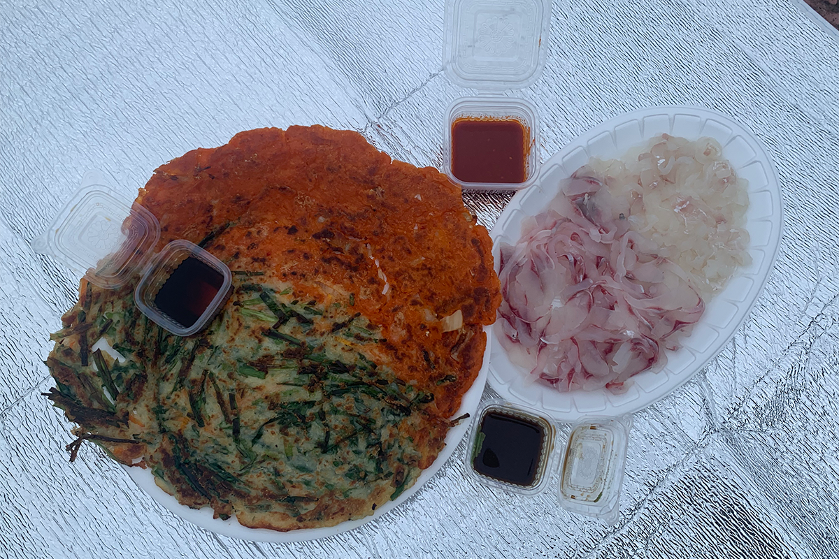 用手抓起一塊韓國煎餅，準備蘸上醬料，充滿韓國街頭小吃的獨特風味。