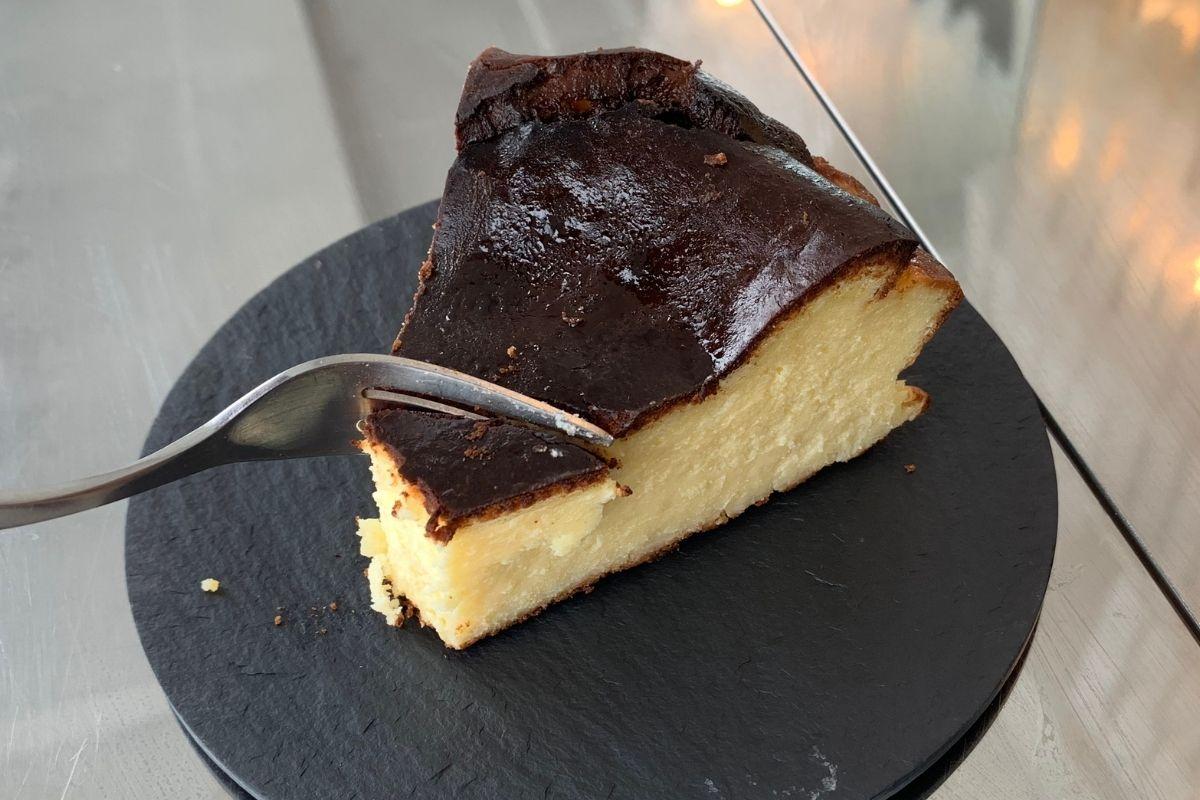 Cafe In Busan cutting Basque Burnt Cheesecake with a fork on a black plate