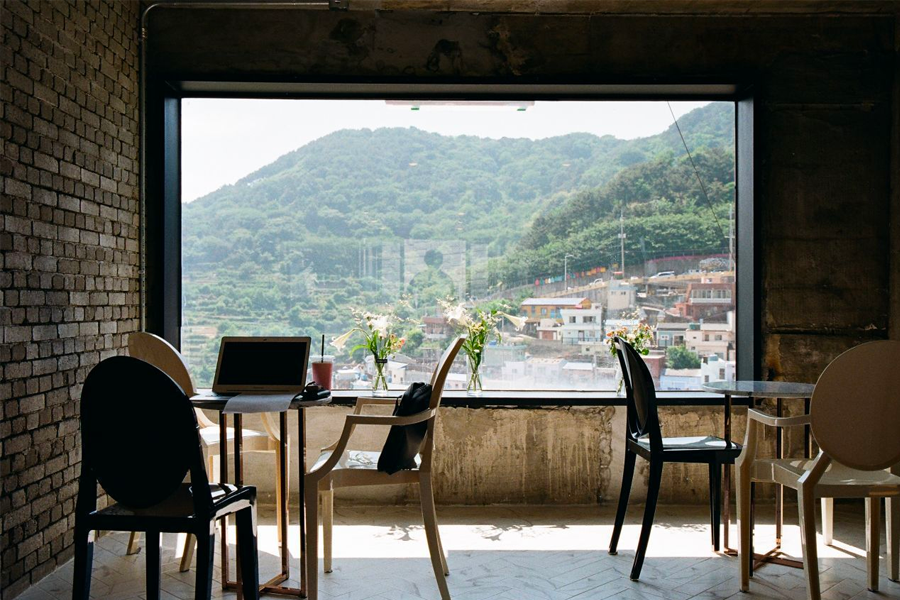 Scenic view from Coffee It House overlooking Gamcheon Culture Village, with comfortable seating and natural light creating a cozy atmosphere.