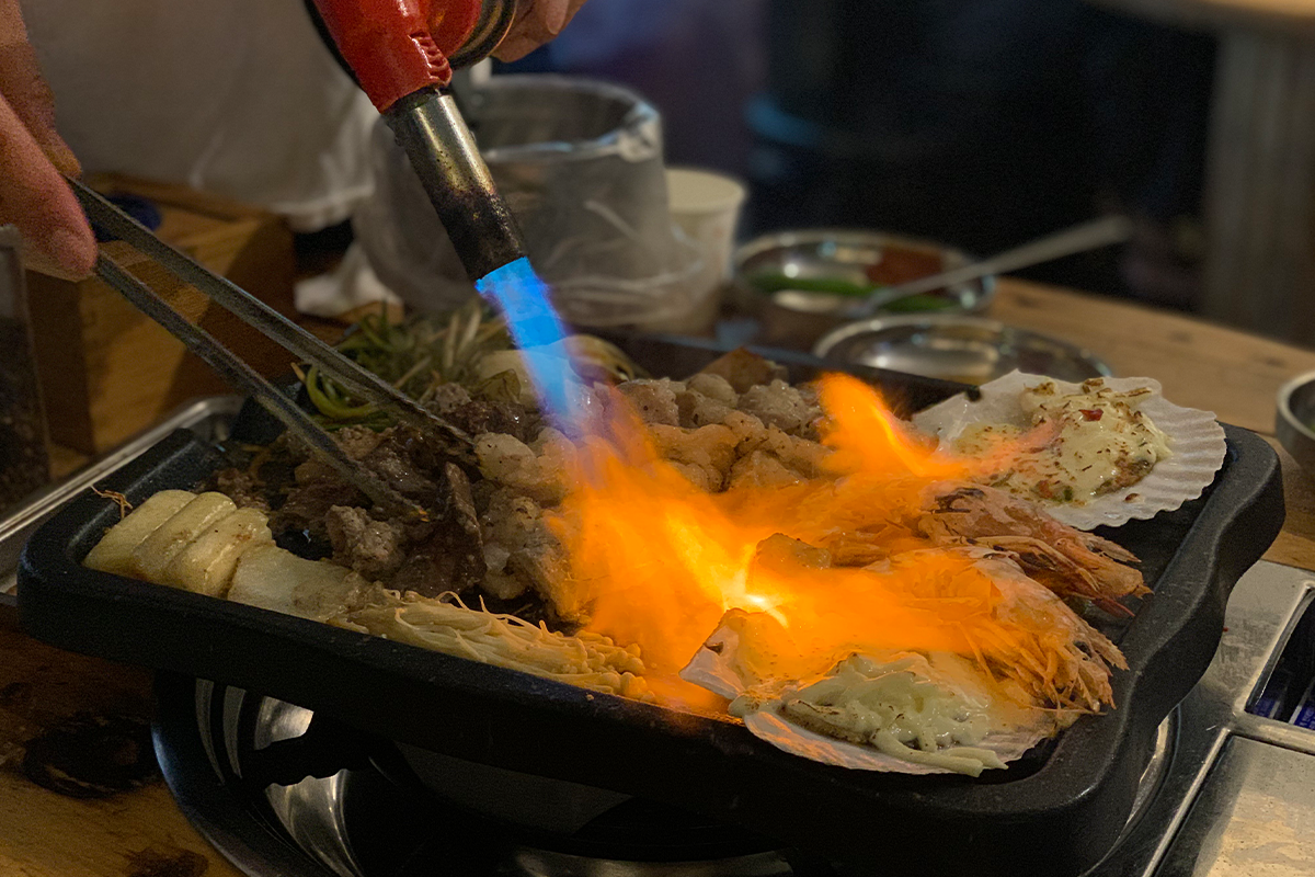 Close up shot of blowtorch being used to cook items on grill
