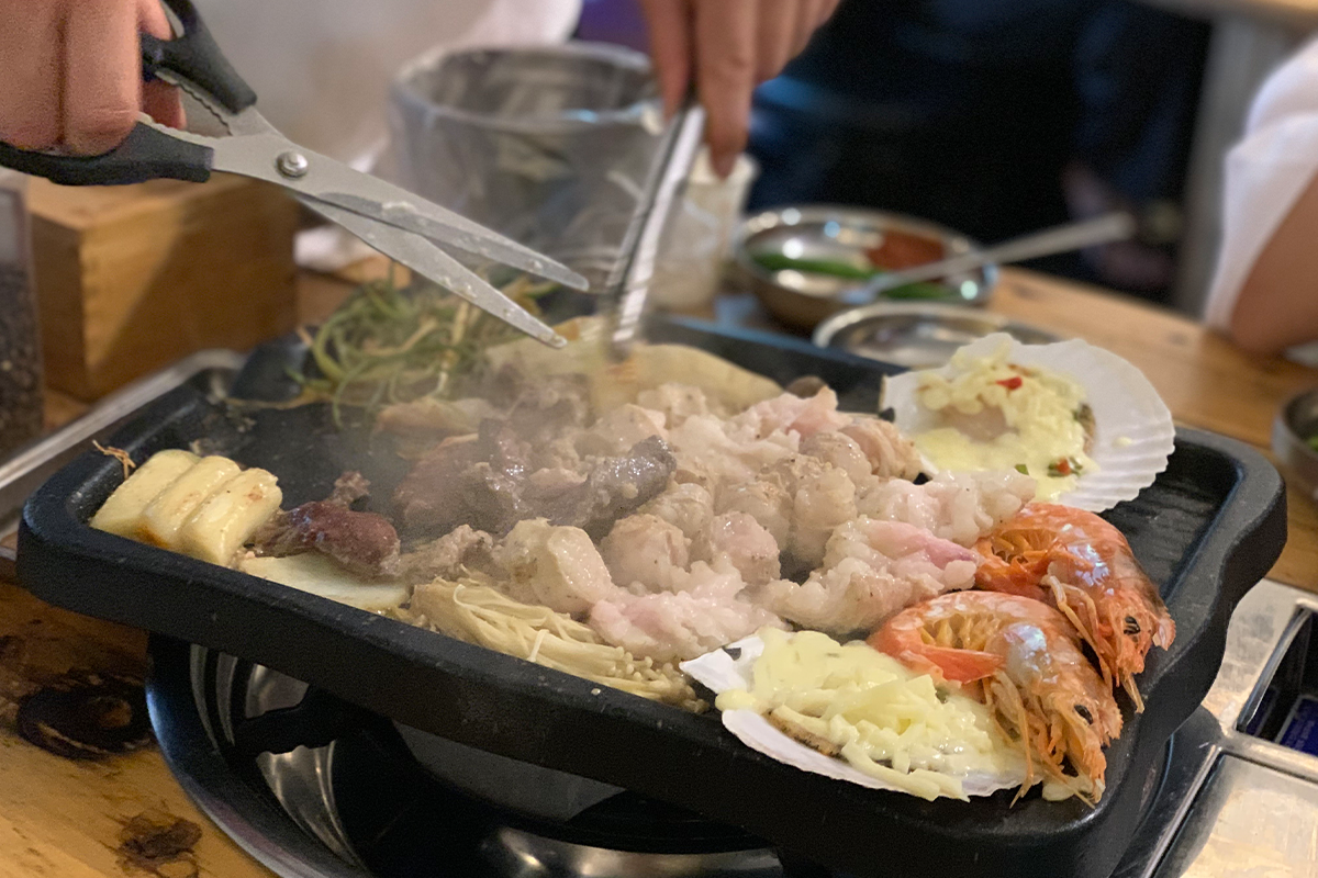 Food cooking on grill and customer cutting grilled items into smaller pieces