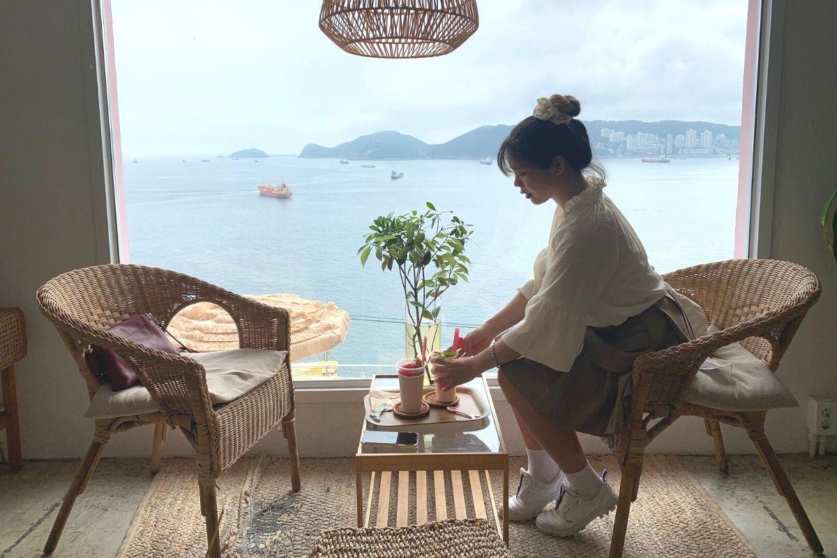白淺灘文化村咖啡館的落地窗視角，藤椅和透明桌子，能看到釜山的海景，完美捕捉度假的感覺。
