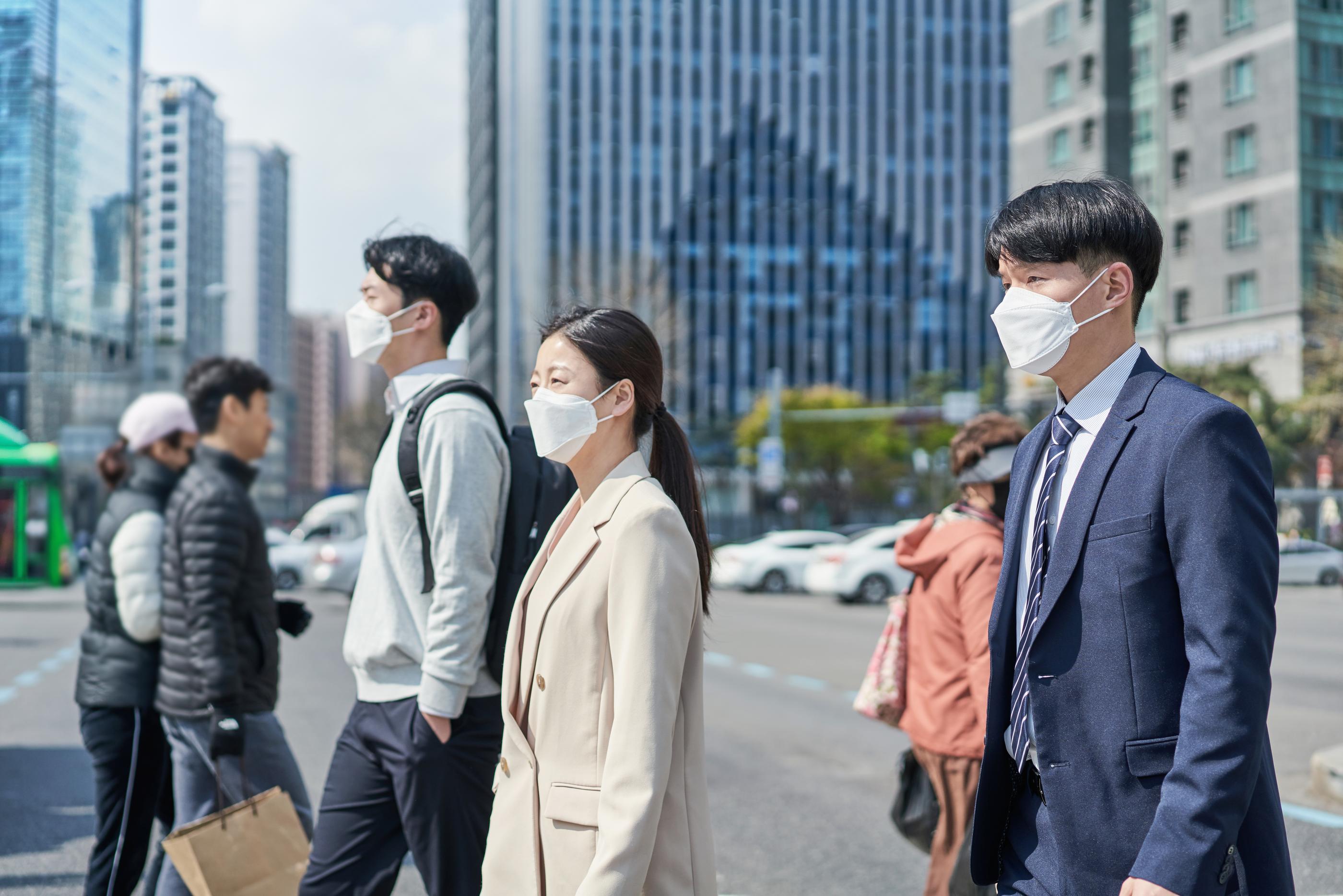men and women crossing the street in Seoul wearing white masks
