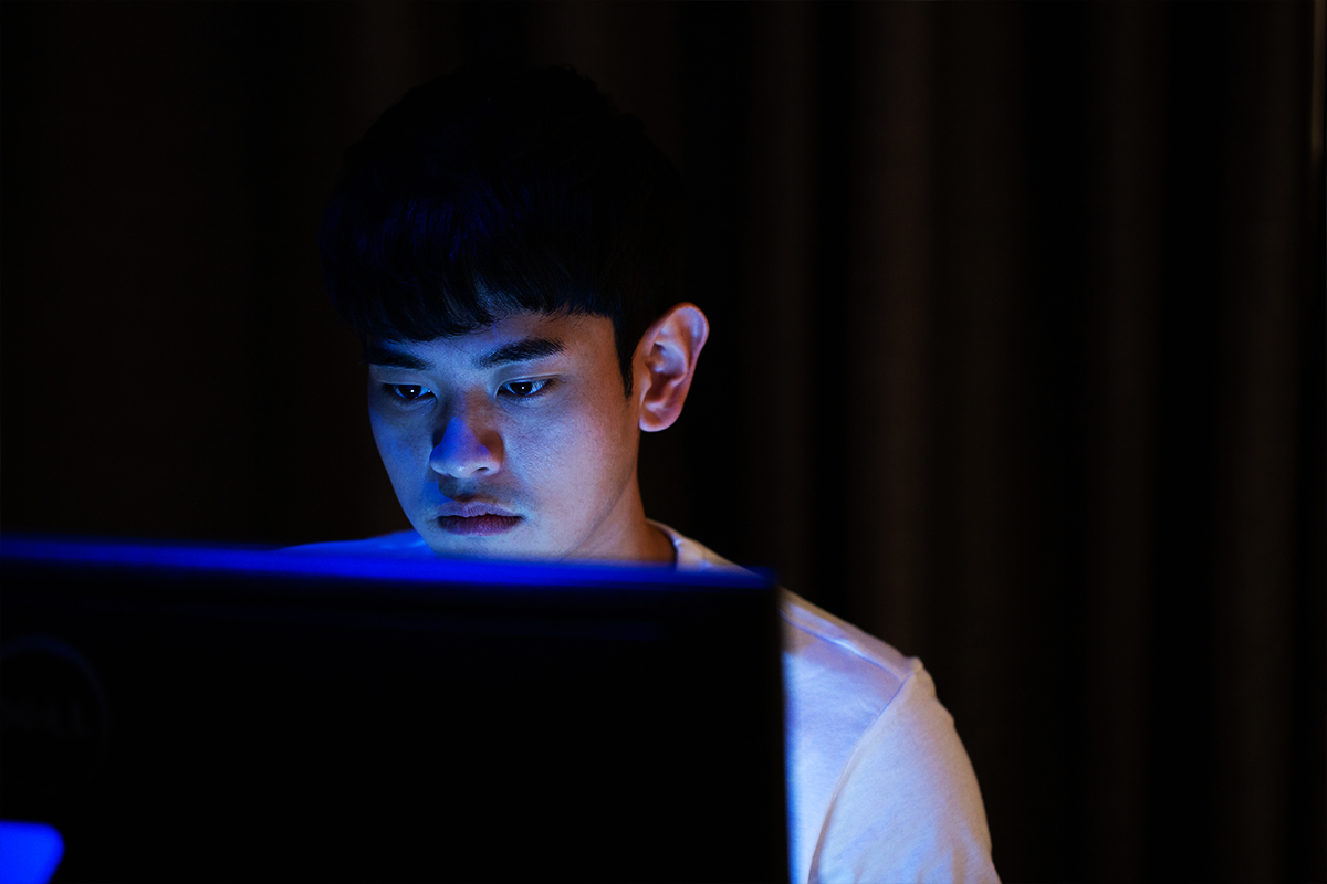 Korean man behind computer screen in the dark with a white T-shirt