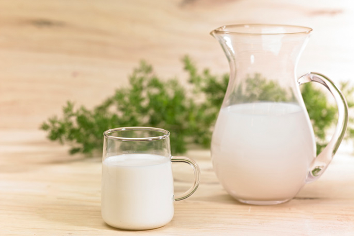 透明玻璃水壺同杯子裝滿咗牛奶，放喺木枱上，強調牛奶中和胃酸嘅效果。