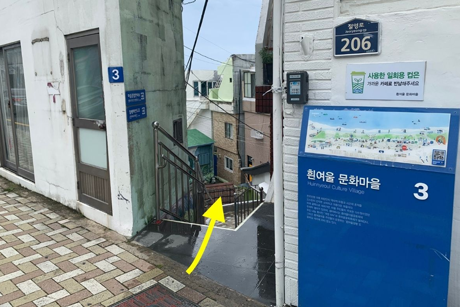 前往白險灘文化村的途中，位於釜山影島的一條小巷，兩旁是當地的住宅建築，遠處可以看到海景。