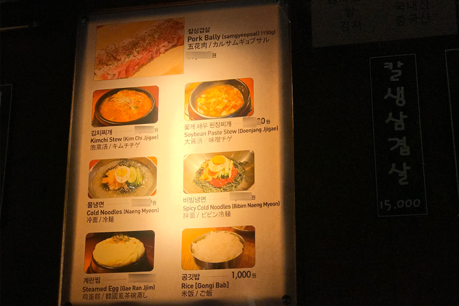 圖片展示了秋風嶺刀五花肉餐廳的牆上菜單，涵蓋韓國五花肉、泡菜鍋、冷麵等特色料理，並附有多語言翻譯，方便國際客人。