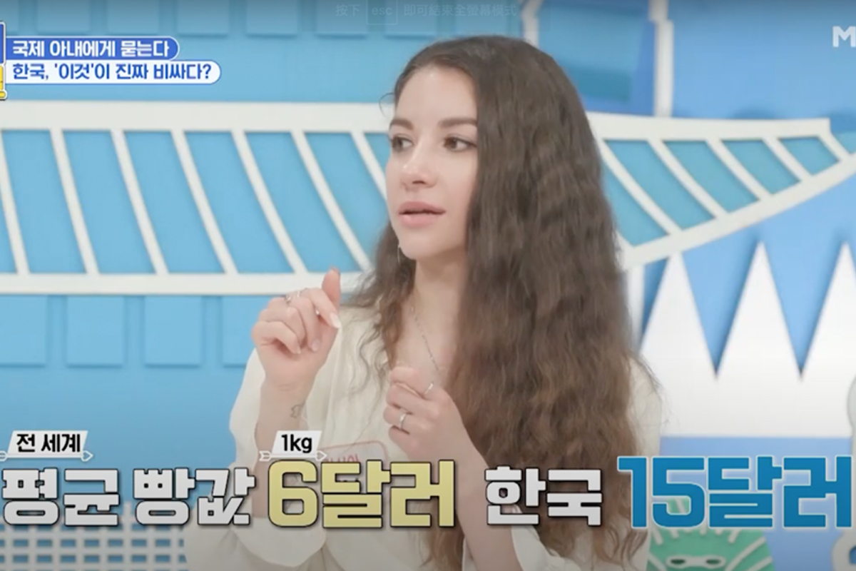 韓國綜藝節目中，一位講者在發言，她面前的螢幕顯示出全球平均麵包價格6美元和韓國的15美元價格對比。