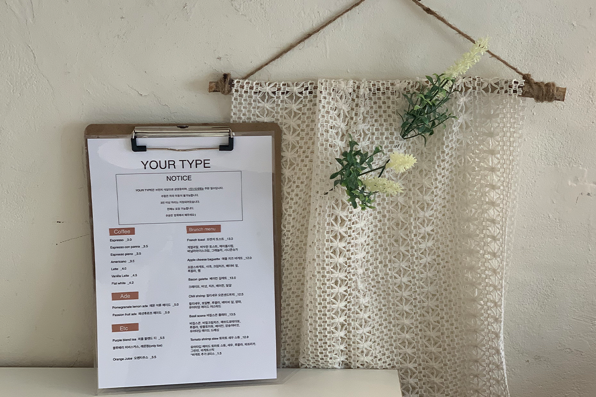 Ansicht der Speisekarte des Your Type Brunch-Restaurants vor einem dekorativen Vorhang an der Wand. Die Speisekarte ist in verschiedenen Sprachen verfügbar, um eine Vielzahl von Kunden anzusprechen.