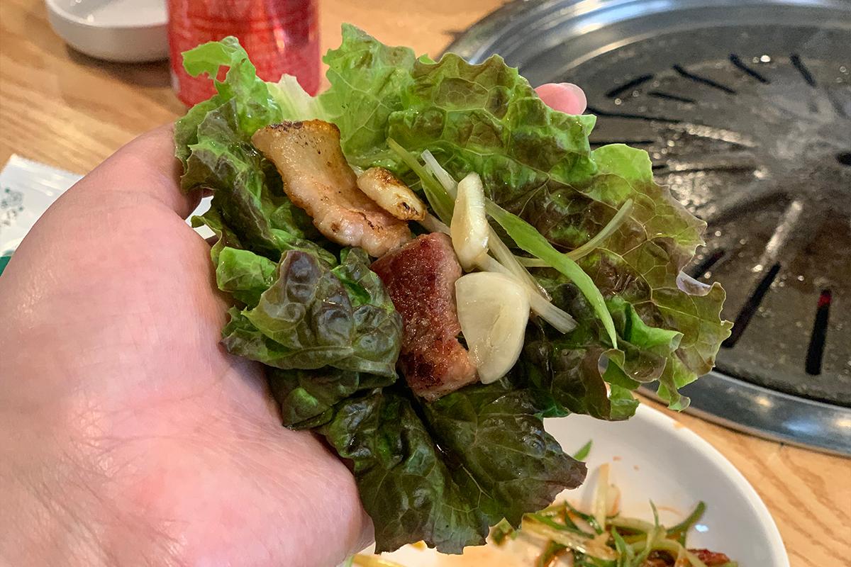 生菜包裹著燒烤豬肉和蒜片，準備入口享用。