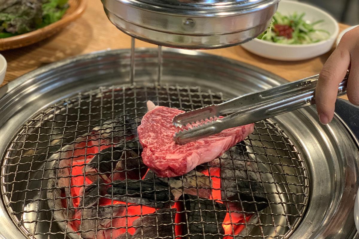 夾取韓牛肉放置於炭火燒烤網上，讓人垂涎欲滴。
