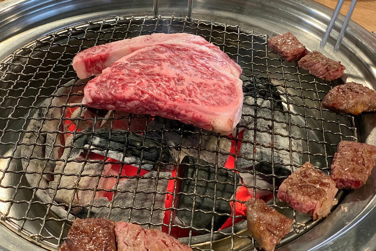 炭火上的韓牛肉，旁邊有一小塊完成品供品嚐。