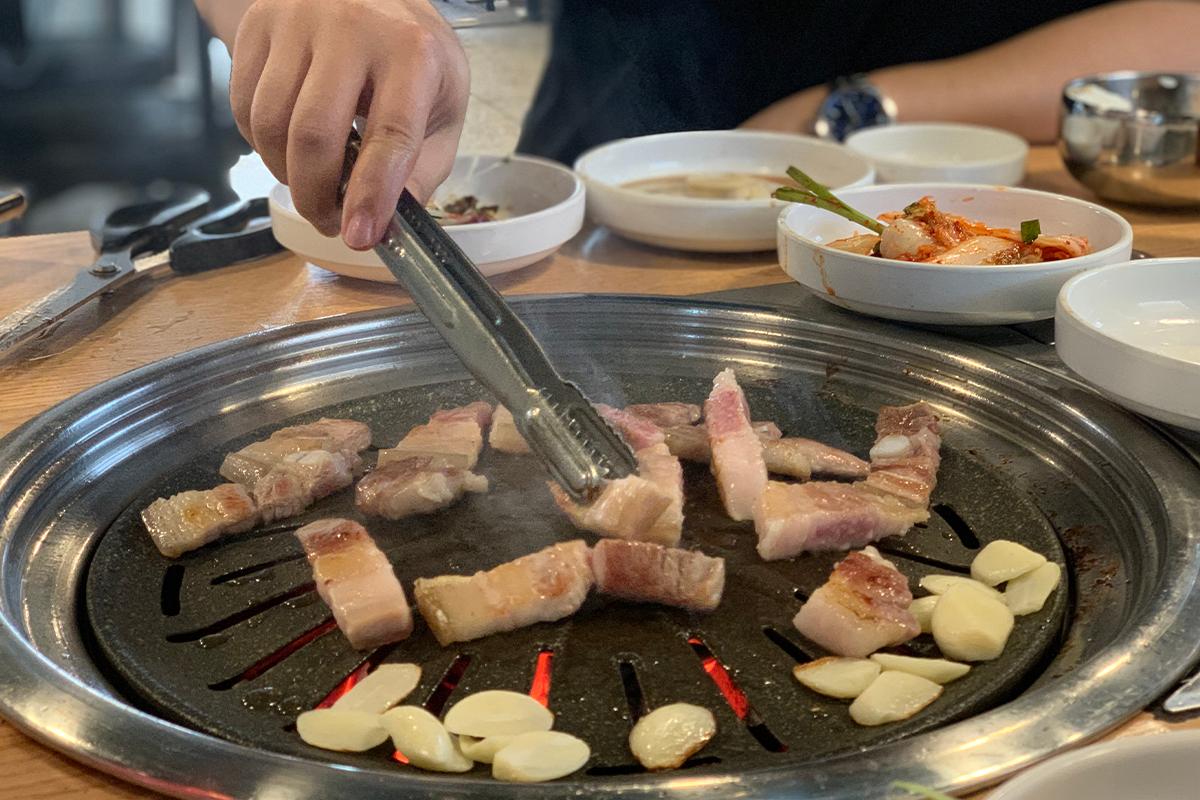 正將五花肉切片在石板上燒烤，充滿從容自得的氛圍。