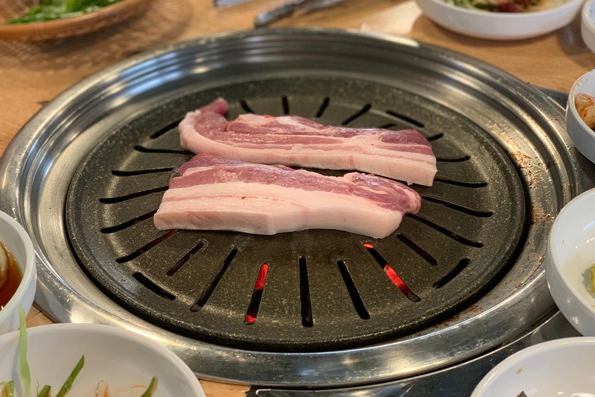 正在石板燒烤的兩片多汁五花肉，散發出誘人香氣。