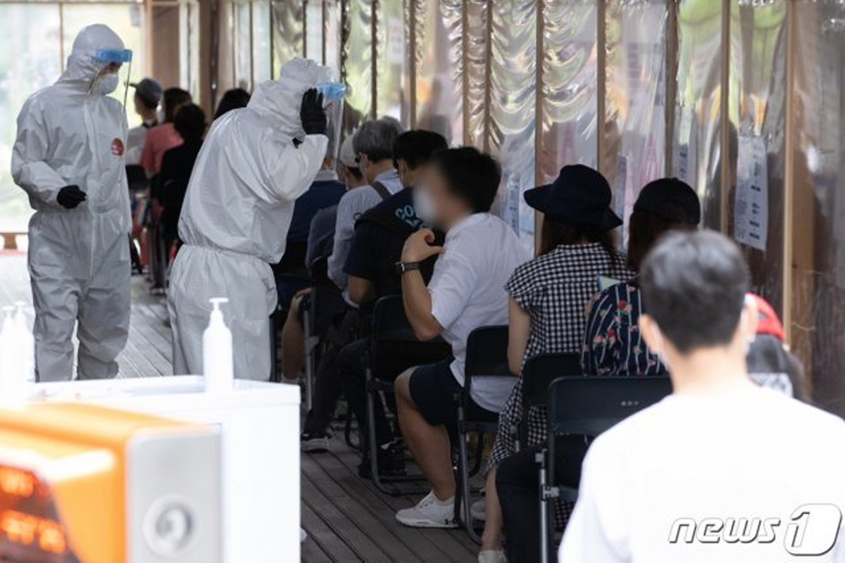 穿著防護服的醫護人員在疫情檢測中心指導排隊的民眾，進行COVID-19檢測。