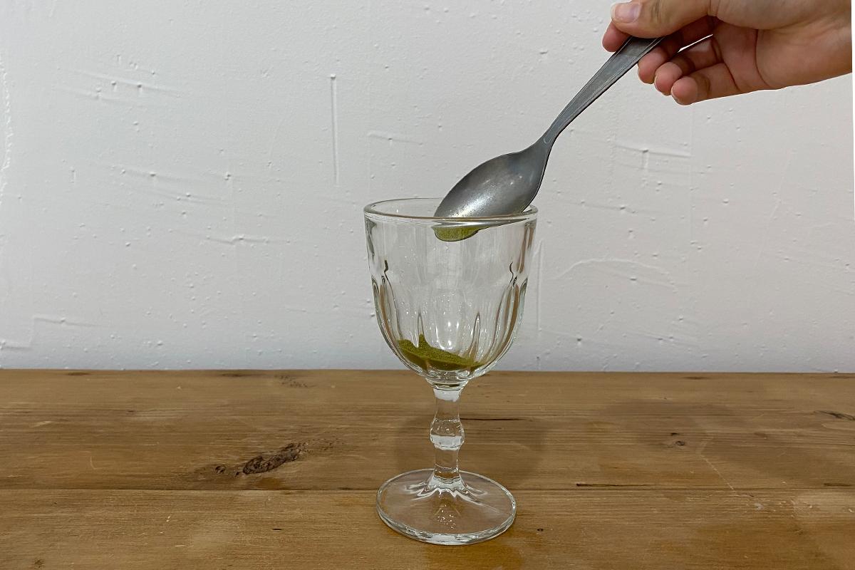 Green tea powder being spooned into glass