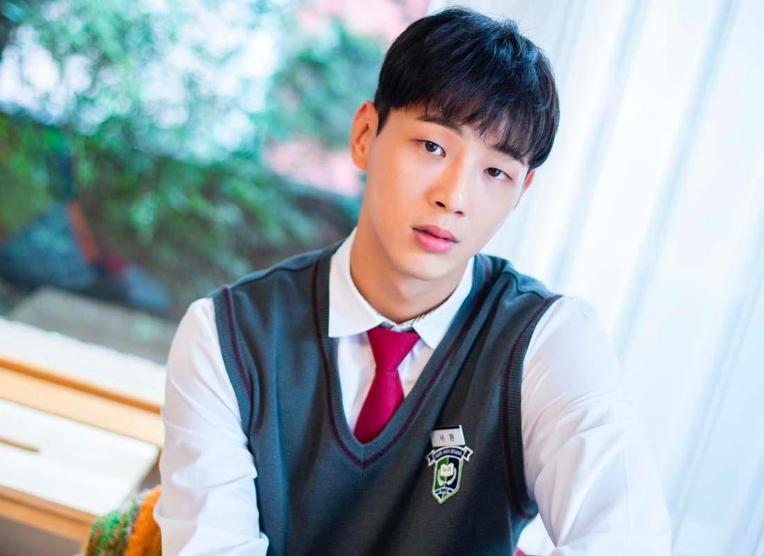 นักแสดงชายสวมใส่ชุดนักเรียนที่มีเสื้อกั๊กสีเทาและเนคไทสีแดงในฉากภาพยนตร์