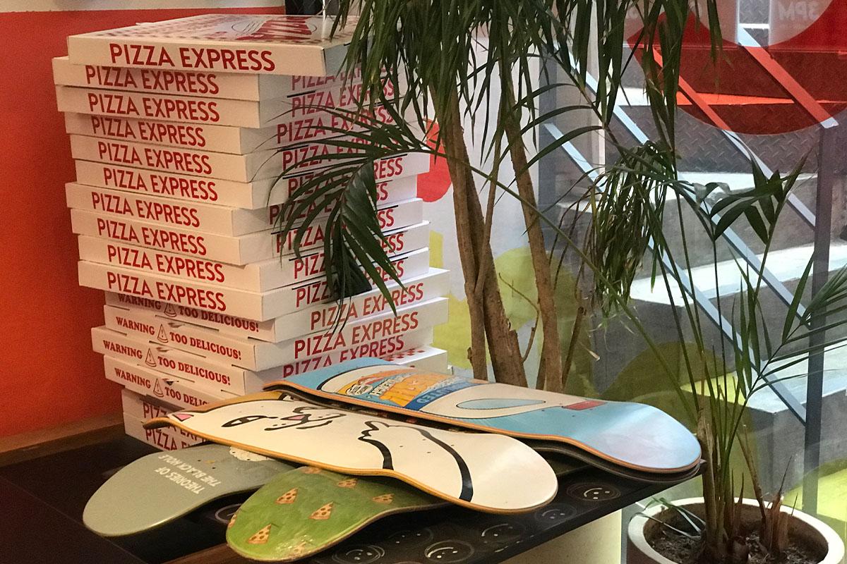 Pizza Express 내부의 스케이트보드 장식과 함께 쌓여 있는 피자 박스들이 있는 사진.