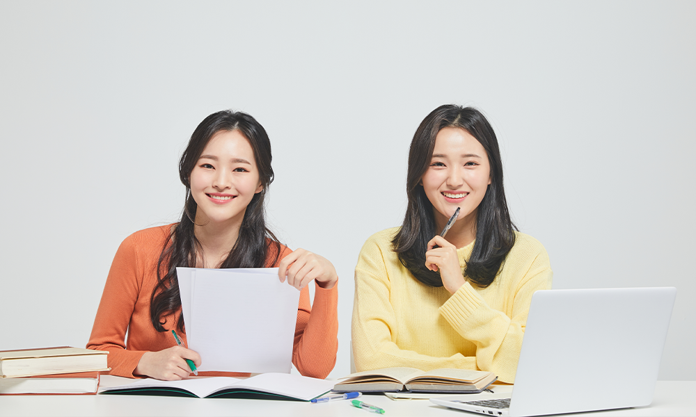 Two Korean girls siting on the desk with laptop and books