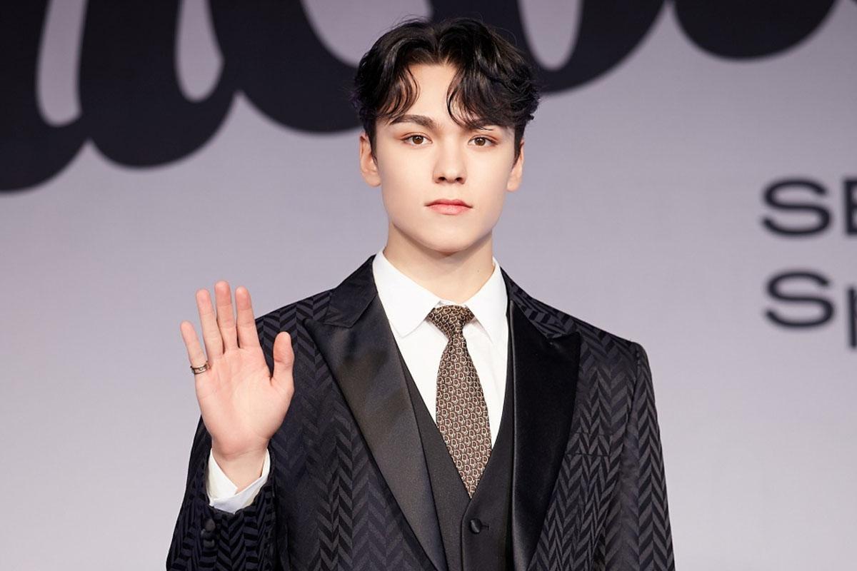 เวอร์น่อนจาก SEVENTEEN ในสูทสีดำและพื้นหลังในงานแถลงข่าว