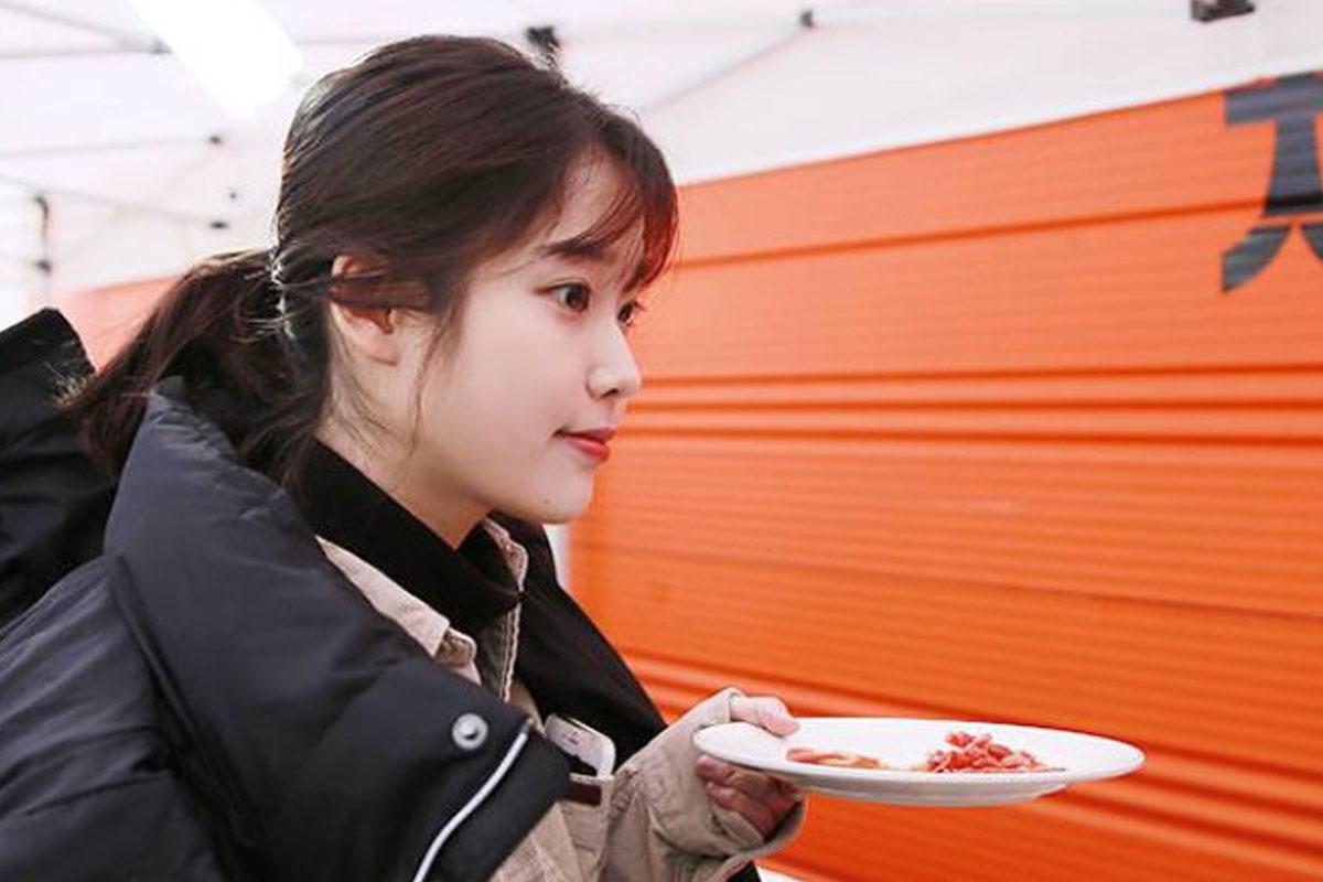 ผู้หญิงถือจานอาหารยืนอยู่ในแนวอาหารกลางแจ้ง