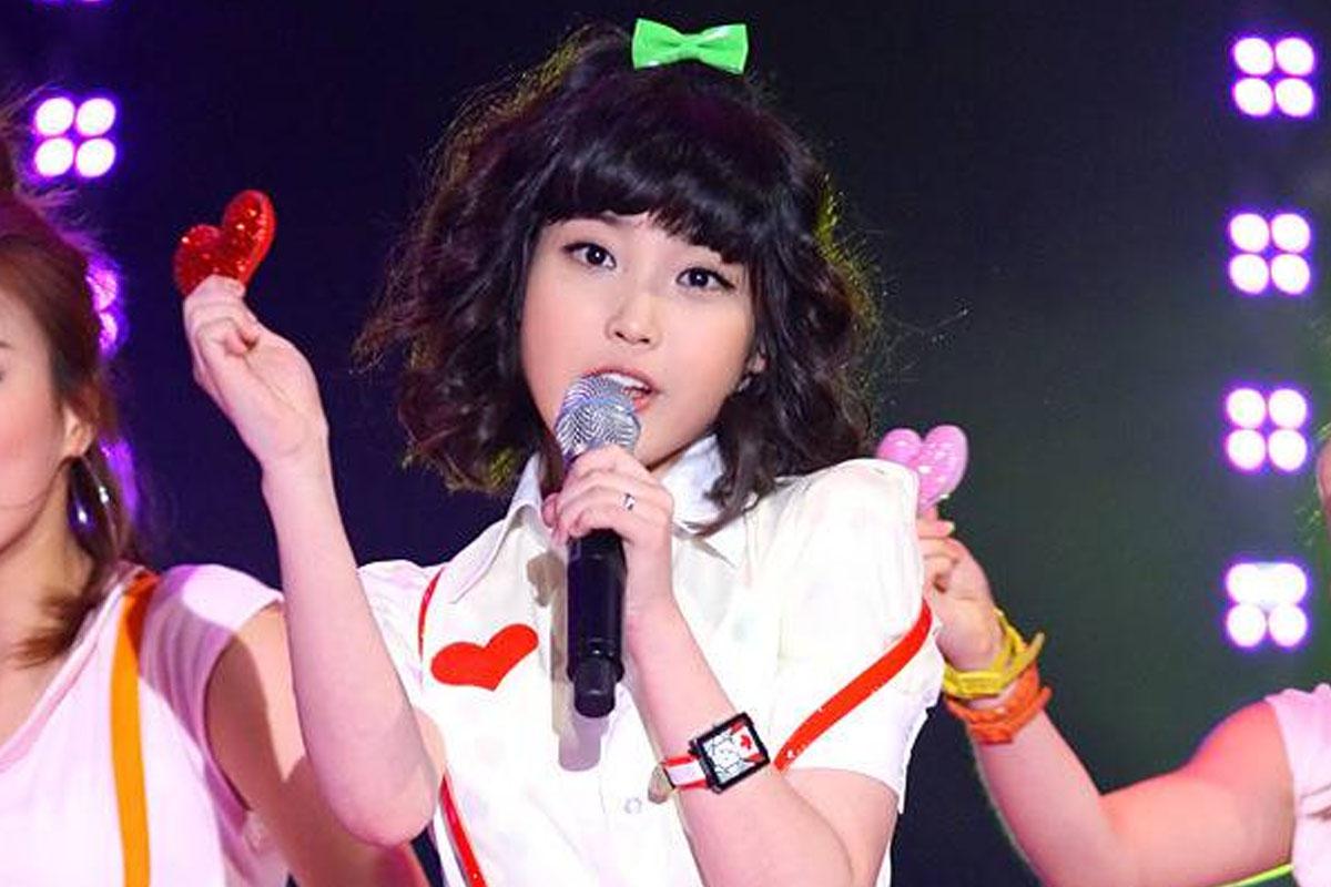 นักร้องหญิงกำลังแสดงบนเวที ถือไพ่รูปหัวใจสีแดงในมือ