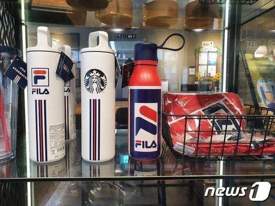 FILAとスターバックスのコラボレーション商品が並んだ店頭ディスプレイ。白いフィラロゴ付きのタンブラーと赤と青の水筒が目立っています。