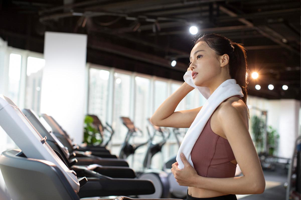 健身房內的跑步機旁，一位女性正用毛巾擦汗，運動後的放鬆時刻。