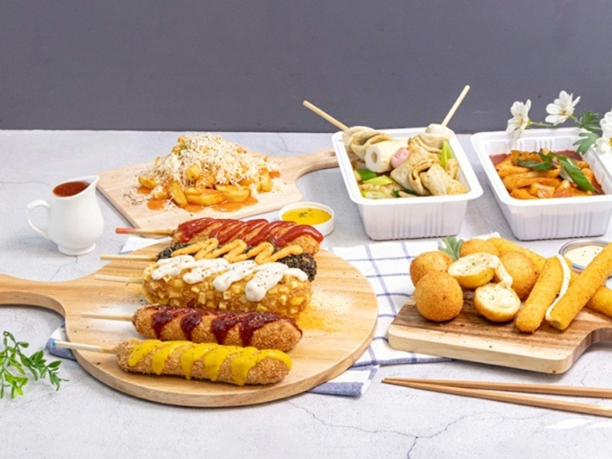 A variety of Korean street food including fish cake hot dogs, tteokbokki, and skewers served on wooden platters.