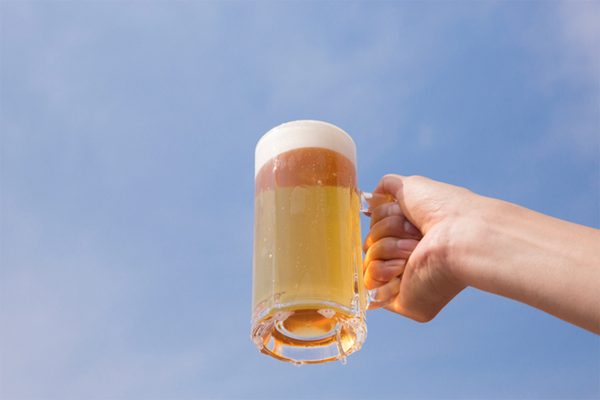 一隻手握住一杯啤酒，啤酒杯呈現泡沫，背景是藍天，展示啤酒杯的典型形狀及其容量。
