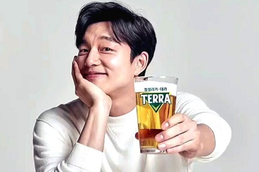 一位身穿白色长袖上衣的人，手持装有淡黄色液体的TERRA品牌啤酒杯。