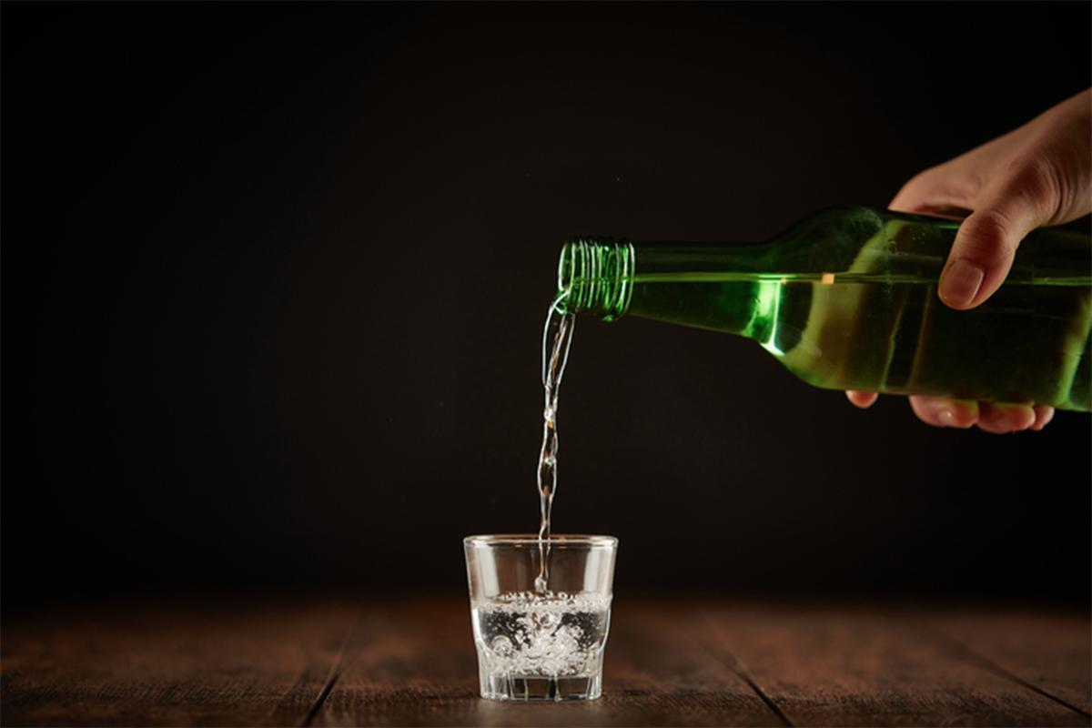 一瓶綠色的瓶子正在傾倒燒酒進入一個小杯中，展示燒酒杯的形狀和適合酒精濃度的容量。