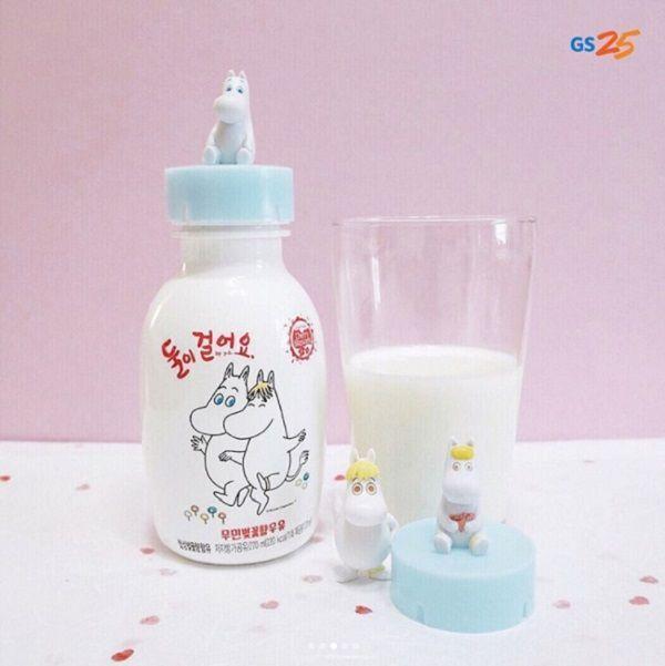 Moomin character figurines seated on blue caps next to decorated milk bottles